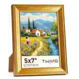 Gold 5x7 photo frame with a colorful landscape painting of houses, flowers, and a stream