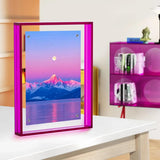 Pink acrylic photo frame displaying colorful mountain landscape on modern desk