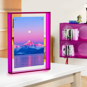 Pink acrylic photo frame displaying colorful mountain landscape on modern desk