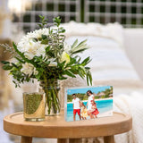 Personalized photo frame with family beach picture on round wooden table next to fresh white flower bouquet, home decor