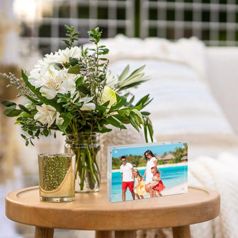 Personalized photo frame with family beach picture on round wooden table next to fresh white flower bouquet, home decor
