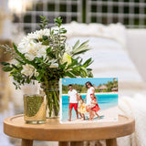 Custom acrylic photo frame with family beach portrait on wooden table beside fresh flower bouquet