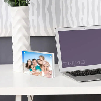 Custom acrylic photo frame with family picture on modern white desk beside laptop and plant