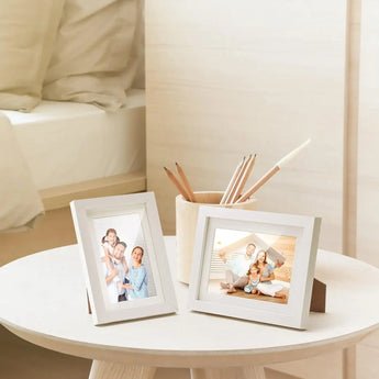 Custom white photo frames with family photos on a round bedside table in a cozy bedroom
