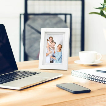 White photo frame with family portrait on modern office desk near laptop and coffee cup