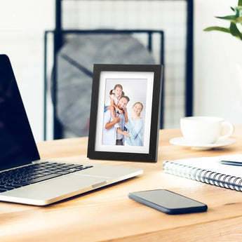 Black photo frame with family portrait on modern desk beside laptop and notebook