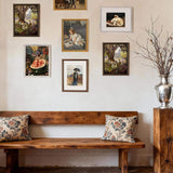 Gallery wall of framed art above rustic wooden bench with floral pillows and decorative vase.