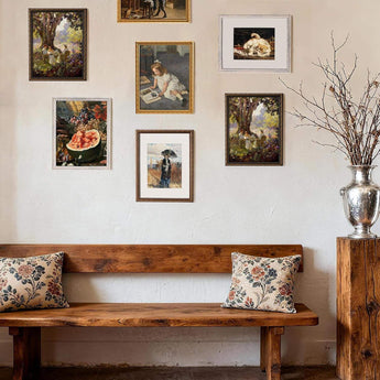 Gallery wall of framed art above rustic wooden bench with floral pillows and decorative vase.