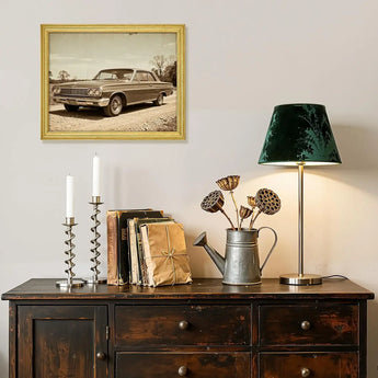 Vintage car wall art in gold frame above rustic sideboard with books, lamp, and decor